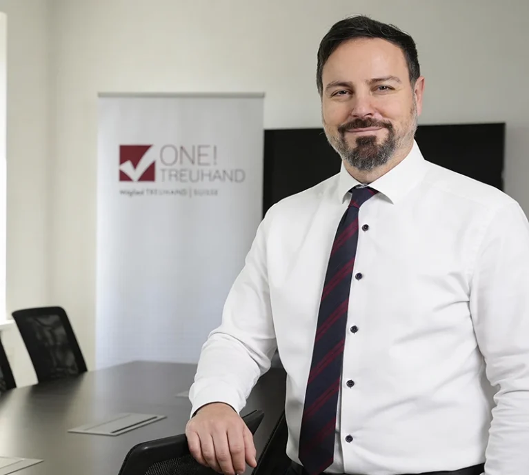 Ein Mann im Business-Outfit vor einem One! Treuhand Banner. Keywords: Treuhand, Steuerberatung, Consulting, Finanzexperte.